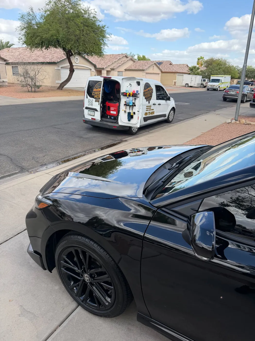 Black Toyota Camry with a ceramic-coated glossy finish next to the Carson's Mobile Detailing van in Arizona