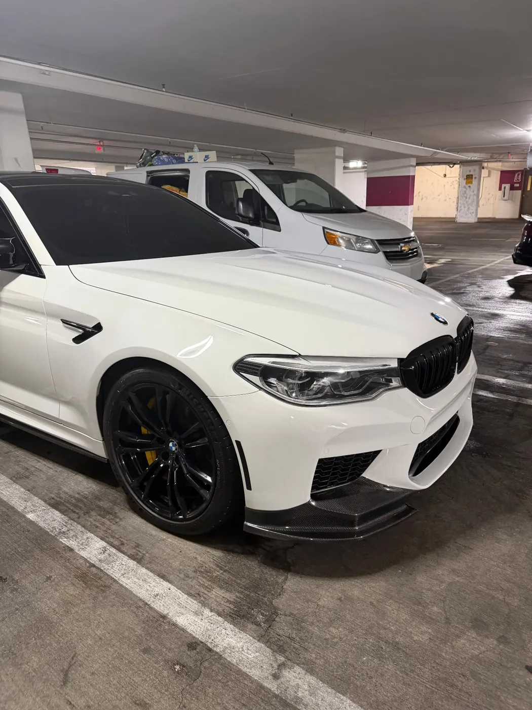 Front three-quarter view of a white BMW M5 with carbon fiber splitter after a mobile detail