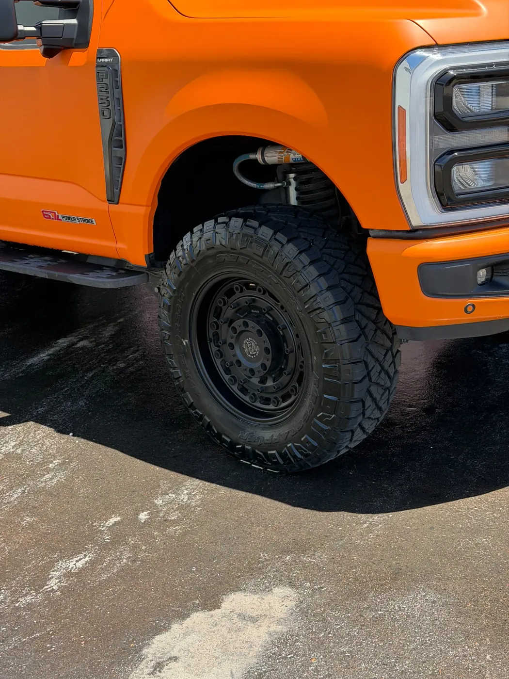 Close-up of a cleaned black off-road wheel and tire on an orange Ford F-250 after mobile detailing